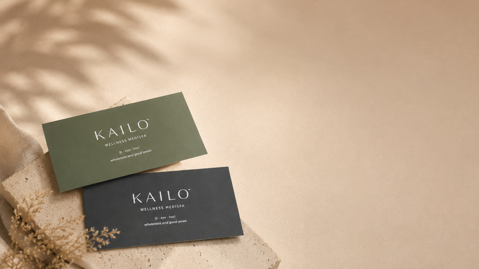 Two Kailo business cards on a beige surface with a natural leaf background